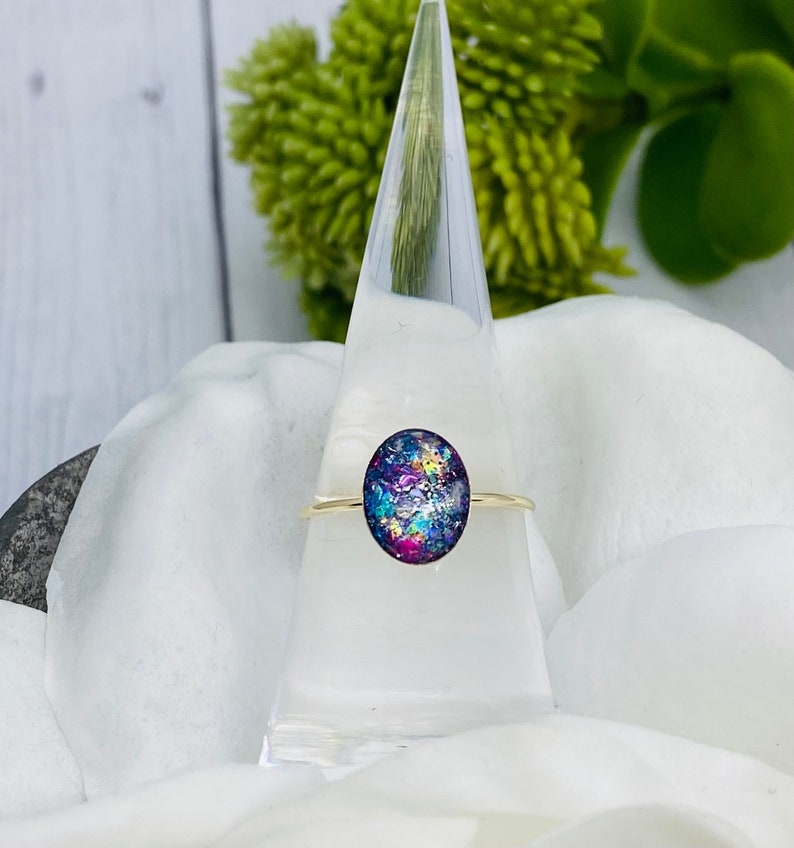 May include: A gold ring with a colorful oval-shaped resin stone. The stone has a blue, purple, and pink color scheme with iridescent glitter.
