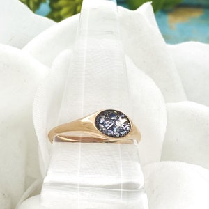 May include: A gold signet ring with a round, dark blue stone set in the centre. The stone is made of iridescent glitter.