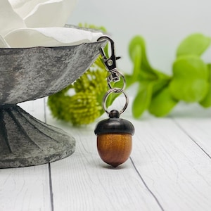 May include: A wooden acorn keychain with a silver metal loop and clasp. The acorn is brown with a dark brown cap.