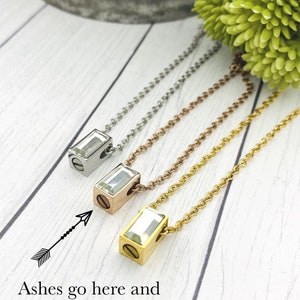 May include: Three necklaces with different colored chains and a clear crystal pendant. The pendant has a screw on the side, and the text "Ashes go here and are hidden in this necklace." is below the image.