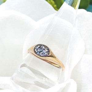 May include: A gold ring with a blue gemstone set in a round bezel. The ring is on a white display stand.