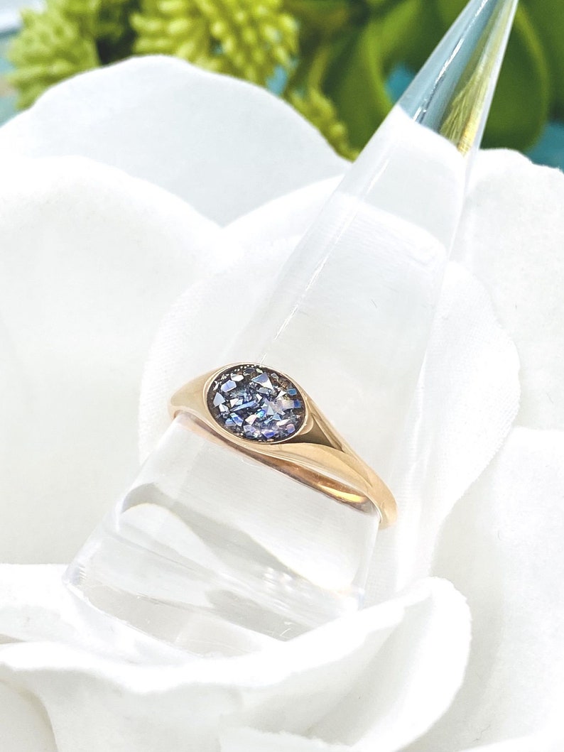 May include: A gold ring with a blue gemstone set in a round bezel. The ring is on a white display stand.