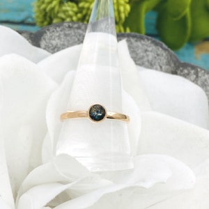 May include: A gold ring with a dark blue and green opal gemstone set in the center.
