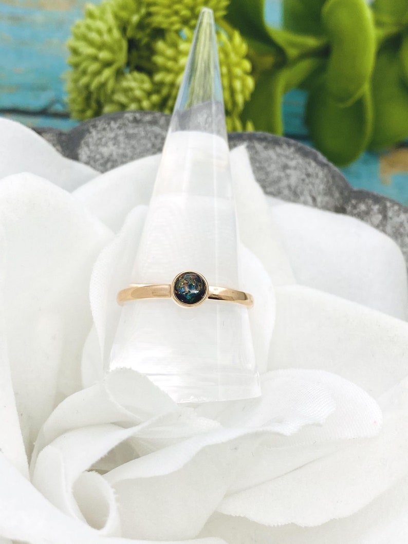 May include: A gold ring with a dark blue and green opal gemstone set in the center.