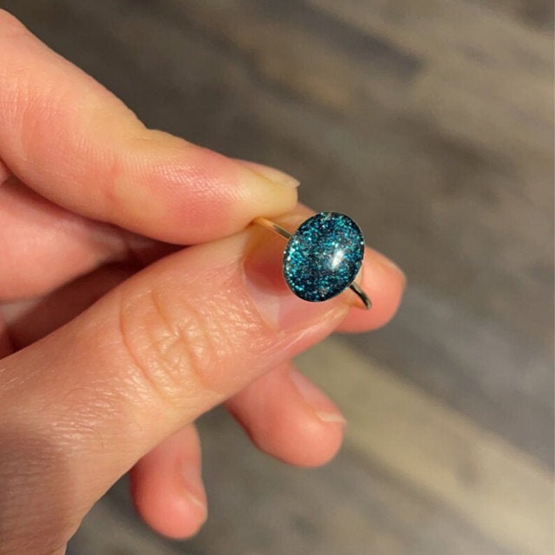 May include: A gold ring with a teal blue oval-shaped stone filled with glitter.