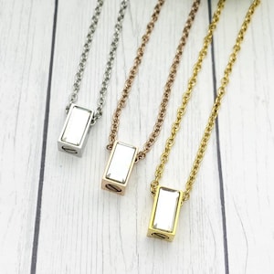 May include: Three silver, gold, and rose gold necklaces with a rectangular pendant featuring a clear crystal. Each necklace has a delicate chain.