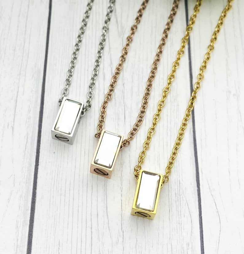 May include: Three silver, gold, and rose gold necklaces with a rectangular pendant featuring a clear crystal. Each necklace has a delicate chain.