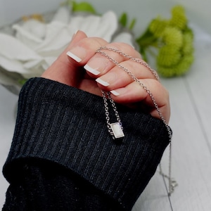 May include: A silver chain necklace with a small rectangular pendant featuring a white stone.