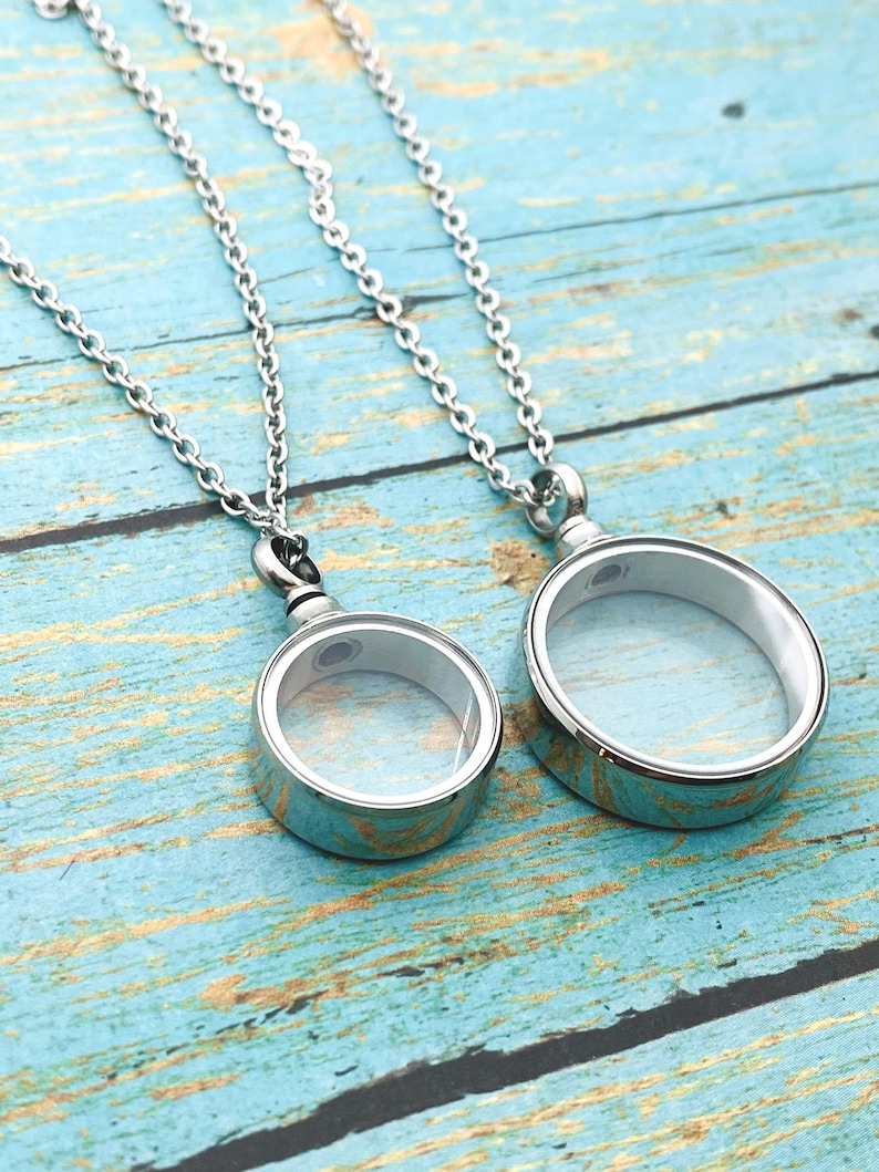 May include: Two silver chain necklaces with round glass pendant charms. The charms are open and have a silver rim.