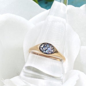 May include: A gold signet ring with a round, iridescent blue stone set in the centre.