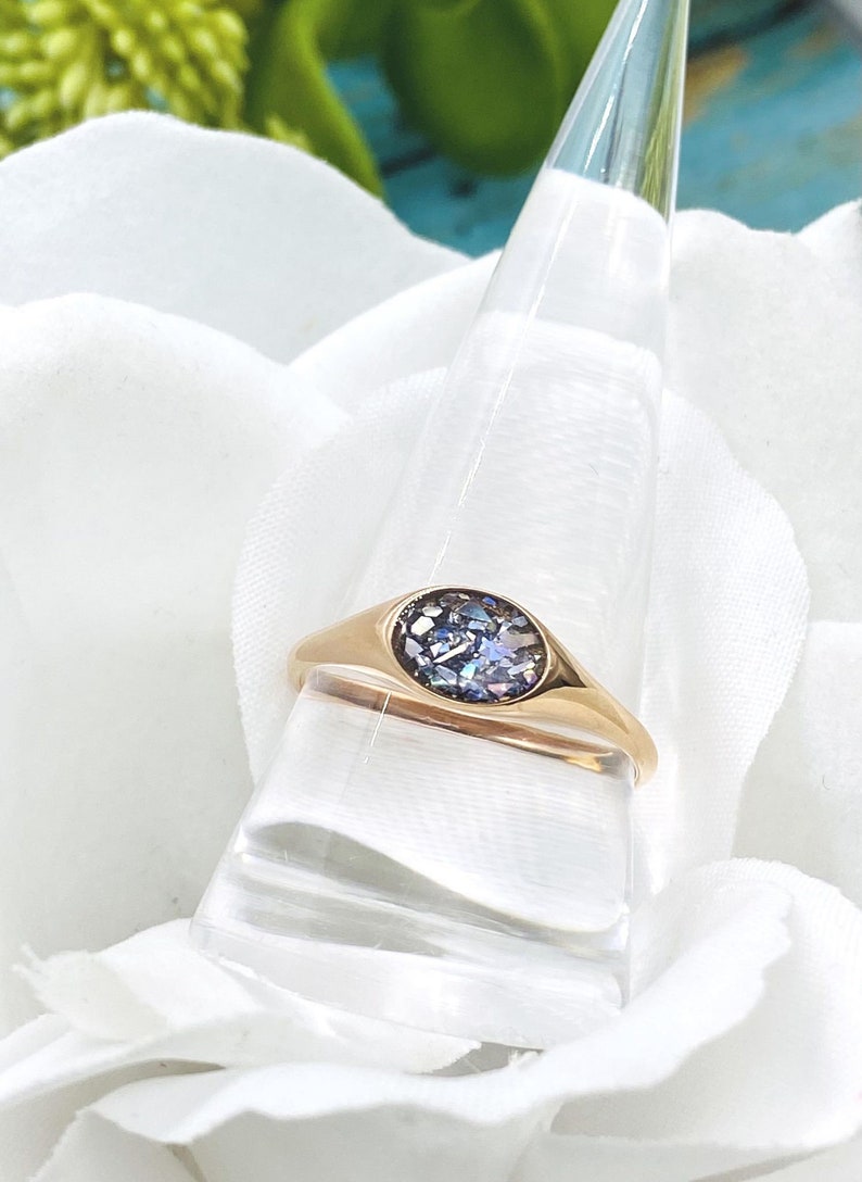 May include: A gold signet ring with a round, iridescent blue stone set in the centre.