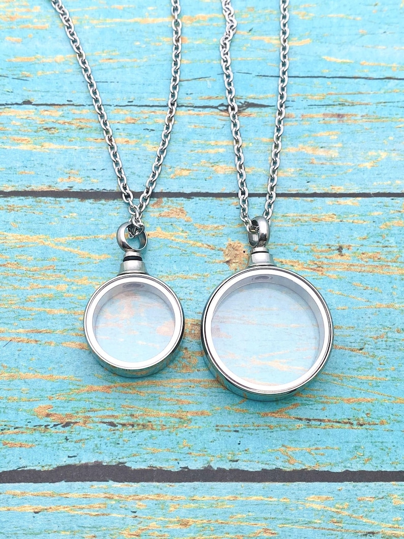 May include: Two silver chain necklaces with round glass locket pendants. The lockets are open and have a clear glass interior.