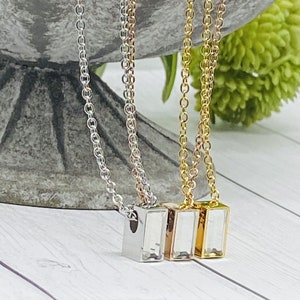 May include: Three silver, rose gold, and gold necklaces with rectangular pendants. Each pendant has a clear crystal inside.