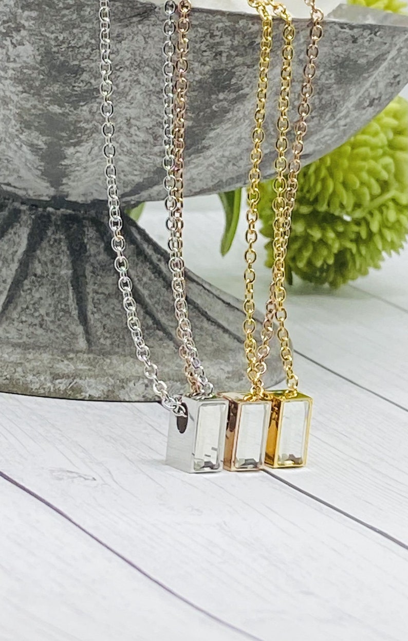May include: Three silver, rose gold, and gold necklaces with rectangular pendants. Each pendant has a clear crystal inside.