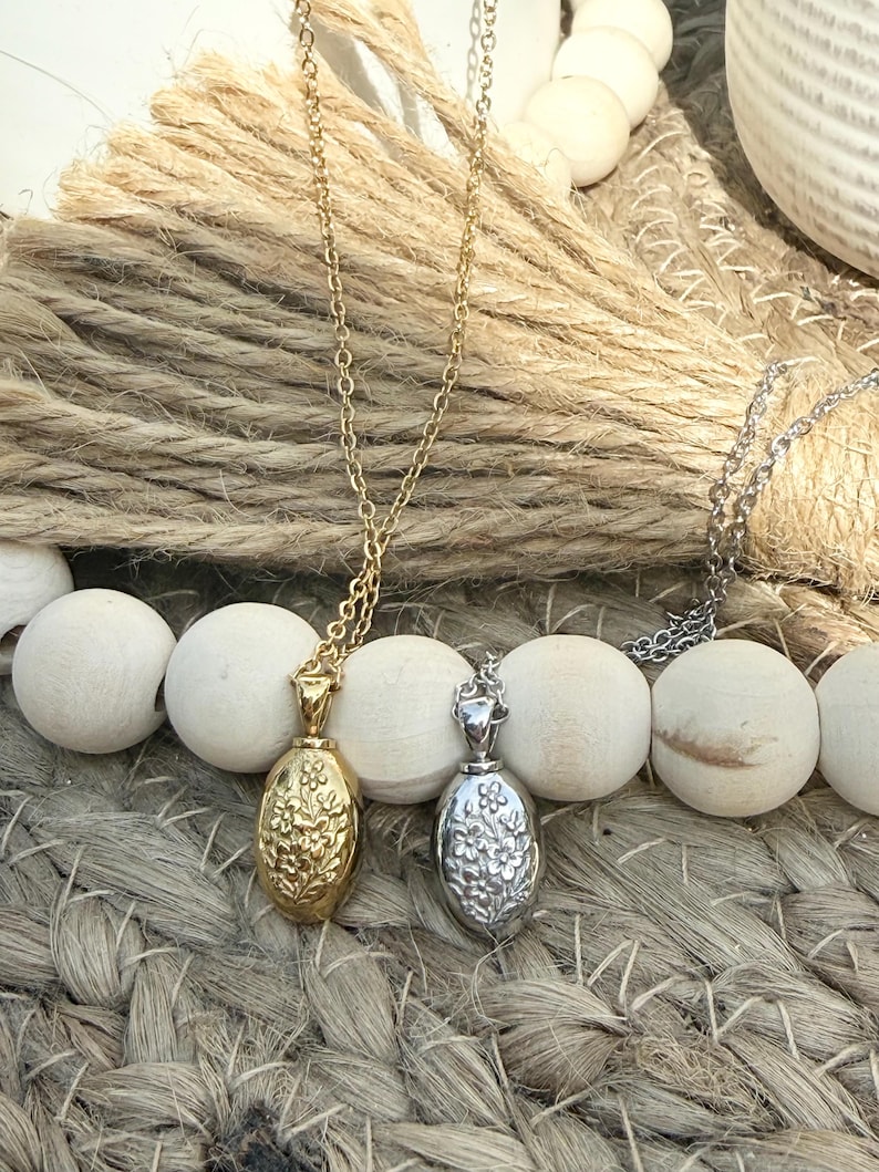 Peut inclure: Deux colliers avec des pendentifs ovales. L'un est dor&eacute; avec un motif floral, l'autre argent&eacute; avec un motif floral similaire. Les deux pendentifs sont suspendus &agrave; de fines cha&icirc;nes. Les colliers reposent sur une surface tiss&eacute;e.