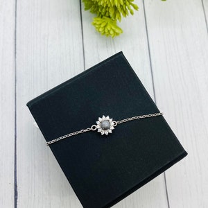 以下が含まれることがあります： 銀色のチェーンブレスレット。中心に灰色の宝石が、銀色の花のデザインで飾られています。