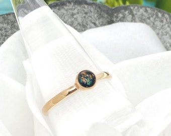 May include: A gold ring with a round, black opal gemstone. The opal has green and gold flecks.