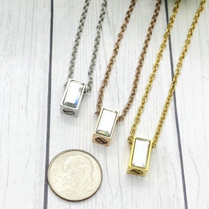 May include: Three silver, rose gold, and gold necklaces with a rectangular pendant featuring a clear crystal. The pendants are about the size of a dime.