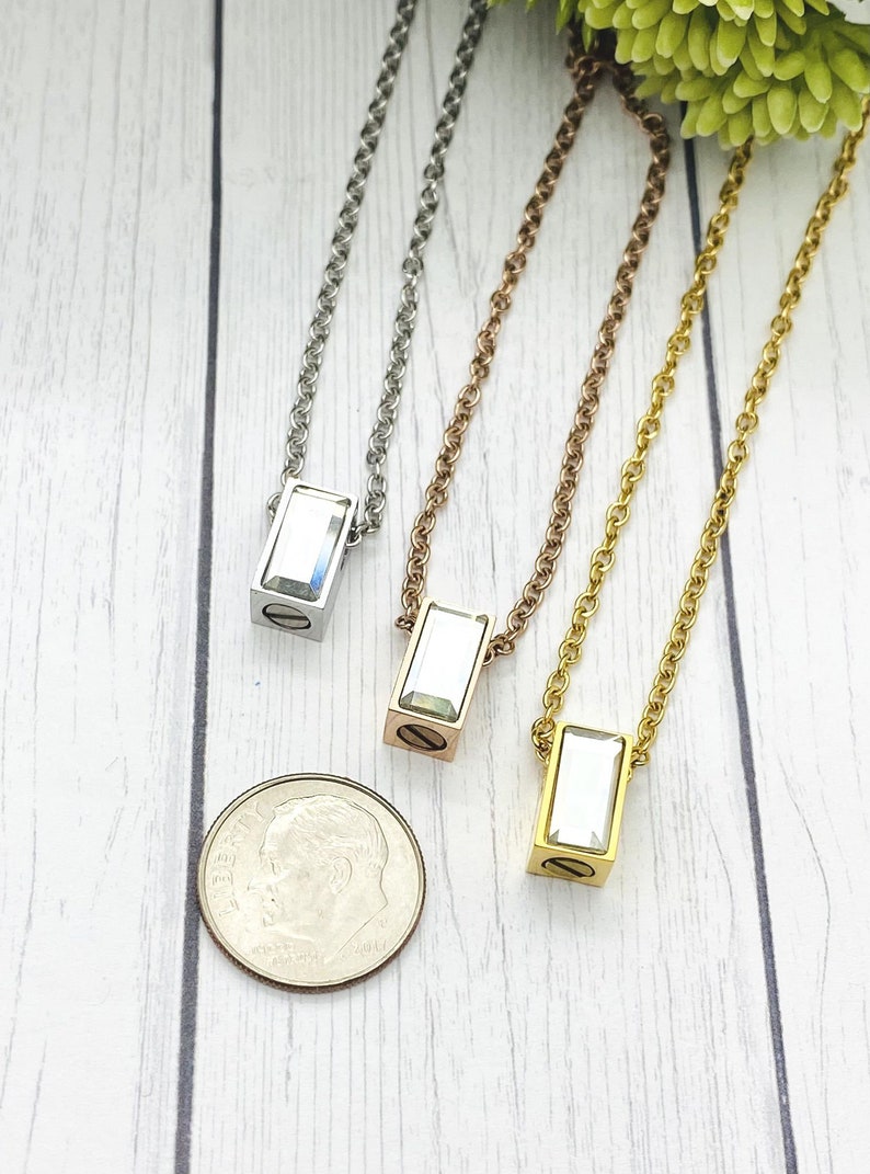 May include: Three silver, rose gold, and gold necklaces with a rectangular pendant featuring a clear crystal. The pendants are about the size of a dime.