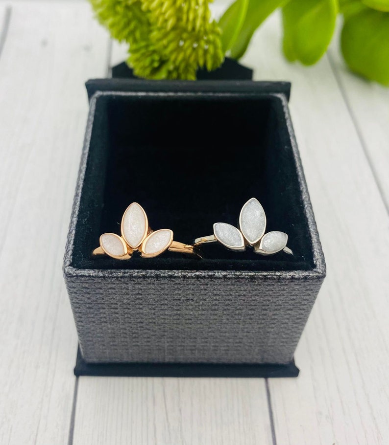 K&ouml;nnte beinhalten: Zwei Ringe mit einem f&uuml;nfbl&auml;ttrigen Blumendesign. Die Ringe sind aus Silber und Ros&eacute;gold und haben wei&szlig;en Glitzer, der in die Bl&uuml;tenbl&auml;tter eingebettet ist.