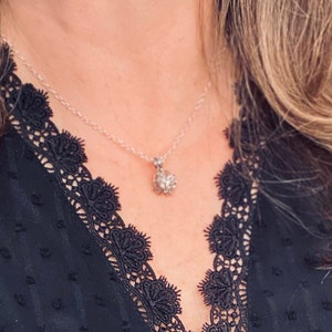 K&ouml;nnte beinhalten: Eine silberne Halskette mit einem kleinen, glitzernden Anh&auml;nger h&auml;ngt an einer Person. Die Kette wird &uuml;ber einem schwarzen Spitzenoberteil getragen.