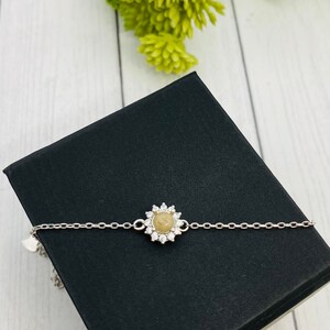 以下が含まれることがあります： 小さな丸い薄い茶色の石が透明なキュービックジルコニアで囲まれた、銀色のチェーンブレスレット。ブレスレットは黒い背景の上に置かれています。