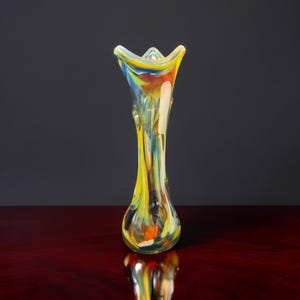 Könnte beinhalten: Eine hohe, farbenfrohe Glasvase mit ausgestellter Oberseite. Die Vase hat einen bauchigen Boden und einen schlanken Hals, mit Streifen in Gelb, Blau und Orange. Die Vase ist etwa 25 cm hoch.