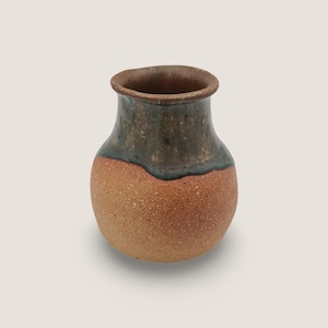 Könnte beinhalten: Eine kleine, handgefertigte Keramikvase mit rundem Körper und schmalem Hals. Die Vase hat ein zweifarbiges Design mit einem rotbraunen Sockel und einem dunkelgrün-braunen oberen Bereich. Der Rand ist dunkler braun. Die Vase hat eine rustikale, erdige Ästhetik.