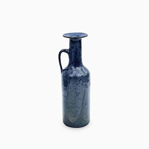 Può includere: Una brocca in ceramica alta con una smaltatura maculata blu scuro e grigia. Il vaso presenta un corpo cilindrico, un manico curvo attaccato al collo e un'ampia apertura con bordo piatto sulla parte superiore, con una finitura lucida.