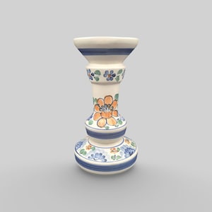 Pode incluir: Um castiçal de cerâmica com base branca, adornado com padrões florais azuis e laranja. O castiçal tem um topo alargado e uma base arredondada, com riscas azuis e detalhes florais. Um acessório decorativo para a casa.