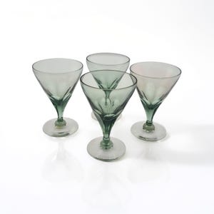Könnte beinhalten: Vier Cocktailgläser im Vintage-Stil mit grünen Stielen und Böden. Die Gläser haben eine konische Schale und bestehen aus klarem Glas mit einem grünen Farbton. Die Gläser sind auf einer weißen Oberfläche angeordnet.