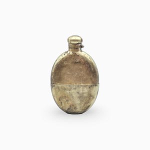 Peut inclure: Une flasque en métal de forme ovale avec une finition dorée ternie. Le récipient présente un corps arrondi et un petit bouchon à vis cylindrique au centre. La surface montre des signes visibles d'usure et de décoloration sur tout l'extérieur.
