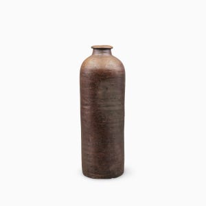 Könnte beinhalten: Eine hohe, zylindrische Keramikflasche mit einer dunkelbraunen, texturierten und verwitterten Oberfläche. Das Gefäß verfügt über einen schmalen Hals, einen flachen, leicht hervorstehenden Rand und einen flachen Boden mit rustikaler Optik.