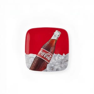 May include: A square ceramic plate featuring a vibrant red background with a graphic illustration of a glass Coca-Cola bottle partially submerged in a pile of clear ice cubes. The bottle displays the white Coca-Cola logo on a red label.