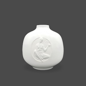 Könnte beinhalten: Eine weiße Keramikvase mit einem glatten, abgerundeten Körper und einem schmalen Hals. In der Mitte der Vase befindet sich ein kreisförmiges Relief einer sitzenden Figur, die eine Kugel und einen Palmwedel hält, in mattem Weiß.