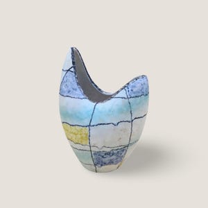 Könnte beinhalten: Eine Keramikvase mit einer einzigartigen, asymmetrischen Form. Die Vase ist mit einem Rastermuster in Blau-, Gelb- und Weißtönen bemalt, wobei schwarze Linien die Quadrate definieren. Die Öffnung ist nach oben gebogen, was das Design künstlerisch macht.