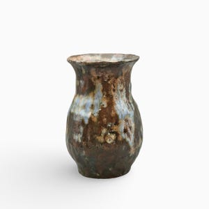 Może przedstawiać: Ceramiczny wazon o pękatym korpusie i rozszerzanym wylewie, pokryty nakrapianym szkliwem w odcieniach głębokiego brązu, ciemnych barw ziemi oraz smugami jasnego błękitu. Powierzchnia ma teksturowane, nierówne wykończenie z widocznymi różnicami w szkliwie.