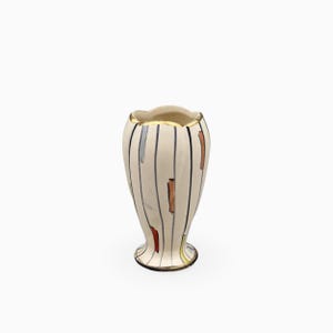 Può includere: Un vaso in ceramica color crema con bordo smerlato e finitura dorata. Il corpo è decorato con linee verticali nere e brevi pennellate rettangolari multicolori sparse in rosso, arancione, blu e giallo.