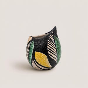 Könnte beinhalten: Kleine, dekorative Keramikvase mit einem einzigartigen Design. Die Vase hat einen schwarzen Hintergrund mit grünen, gelben und weißen geometrischen Mustern. Sie hat eine kleine Öffnung und eine spitze Spitze.