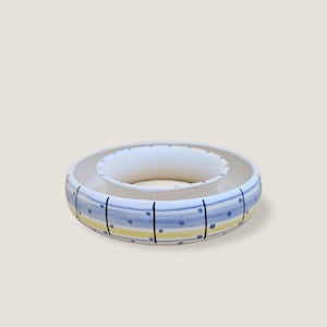 Könnte beinhalten: Ein zweistufiges Serviergeschirr aus Keramik. Der äußere Ring ist mit blauen Streifen, gelben Streifen und blauen Punkten verziert. Der innere Ring ist schlicht weiß. Das Geschirr ist zum Servieren von Dips und Snacks gedacht.