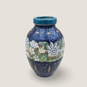 Op de afbeelding: Een keramische vaas met een donkerblauwe achtergrond en een bloemenontwerp. De bloemen zijn wit, groen en bruin. De rand van de vaas is blauwgroen.