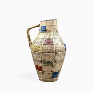 Peut inclure: Un pichet en céramique avec une base beige texturée présentant un motif de grille en relief. La surface est décorée d'accents carrés dispersés en bleu, rouge, jaune et vert, chacun contenant des motifs géométriques linéaires ou tourbillonnants.
