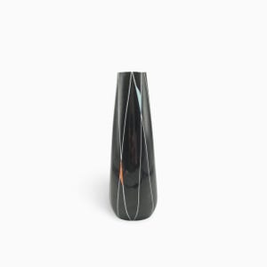Può includere: Un vaso nero alto e affusolato caratterizzato da una serie di sottili linee verticali bianche che creano un motivo a losanga allungato. Il design include piccoli e sottili accenti di forme azzurre e arancioni tra i segmenti delle linee.