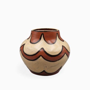 Może przedstawiać: Zaokrąglony ceramiczny wazon z szerokim otworem i zwężaną podstawą. Zewnętrzna powierzchnia ozdobiona jest powtarzającym się wzorem w kształcie łuków w kolorze terakoty i kremowym, obrysowanym cienkimi, ciemnobrązowymi, ręcznie malowanymi liniami.