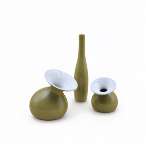 Op de afbeelding: Een set van drie keramische vazen met een gladde olijfgroene buitenkant en een contrasterende witte binnenkant. De collectie bevat één hoge, slanke flesvormige vaas en twee kortere, ronde vazen met brede, uitlopende openingen aan de bovenkant.
