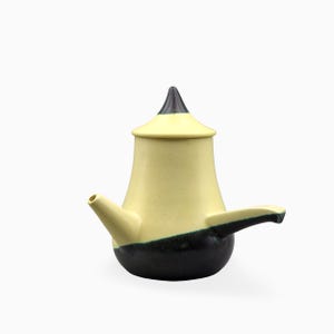 Può includere: Una teiera in ceramica dal design bicolore, con una sezione superiore giallo pallido e una sezione inferiore grigio scuro. Il contenitore presenta un coperchio appuntito con la punta scura, un beccuccio corto e un manico laterale orizzontale.