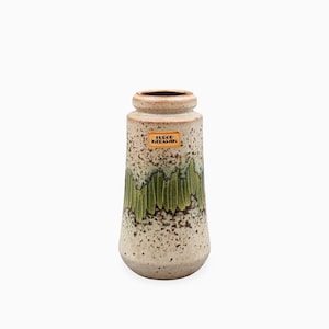 May include: A cylindrical ceramic vase with a speckled beige and brown finish, featuring a prominent band of vertical green drip glaze patterns around the center. An orange rectangular label with the text EUROP KERAMIK is attached to the upper body.