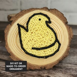 May include: A yellow chick shape created with string art on a wooden slice. The chick is outlined in black string. The wooden slice has a natural wood grain. The text "DIY KIT OR MADE-TO-ORDER ORNAMENT" is on a black rectangle below the wooden slice.