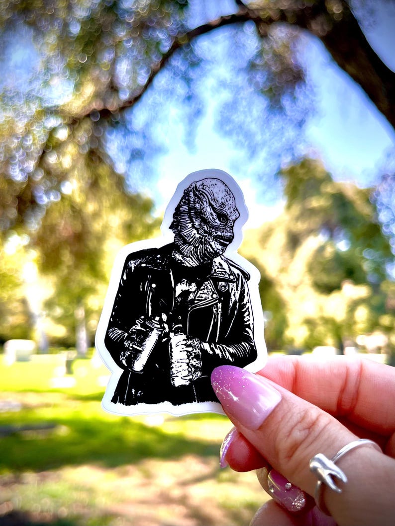 May include: A die-cut sticker featuring a black and white graphic illustration of a creature with textured, scaly skin wearing a leather jacket. The creature is depicted from the chest up, showcasing detailed linework on the face and clothing.