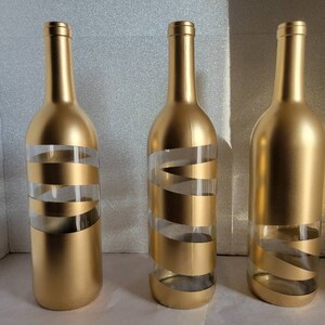 May include: Three gold glass bottles with a clear spiral design. The bottles are empty and have a gold metallic finish.